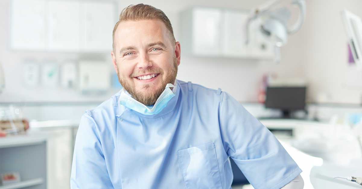 a young dentist smiles at work. improving his emotional health has made a day at the office less stressful